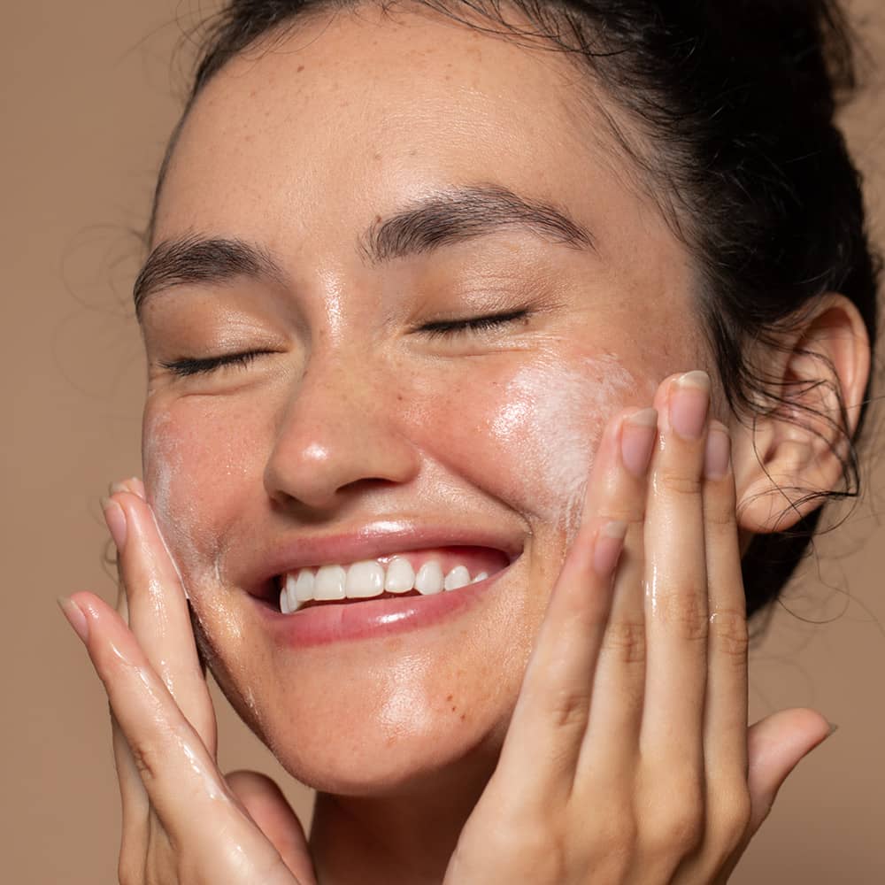 Young smiling woman applying facial wash to cheeks with fingertips