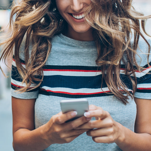 Smiling woman with long blond hair in grey top looking at smartphone