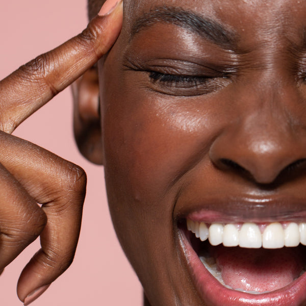 Smiling woman with eyes closed and finger to temples, radiant glowing healthy skin